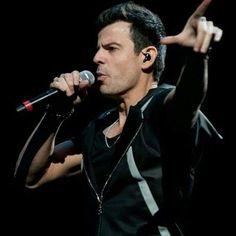 a man holding a microphone in his right hand and pointing to the side with both hands