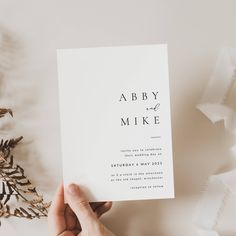 someone holding up a wedding card with the word aby mike on it in front of some leaves