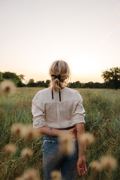 a woman standing in tall grass with her back to the camera