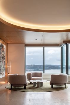 a living room filled with furniture next to large windows overlooking the water and mountains in the distance