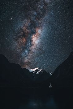 the night sky is filled with stars above mountains and water, as seen from across the lake