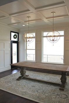 a large wooden table sitting in the middle of a living room with two chandeliers hanging from it's ceiling