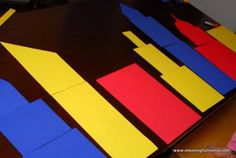 the table is made out of construction paper and has blue, yellow, red, and orange shapes on it