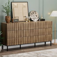 a wooden dresser sitting on top of a hard wood floor next to a lamp and potted plant