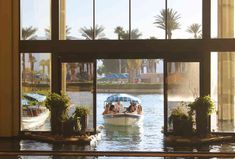 a boat traveling down a river next to a tall building with lots of windows on each side