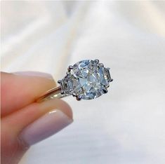 a woman's hand holding an engagement ring with a diamond in the center and two baguetts on each side