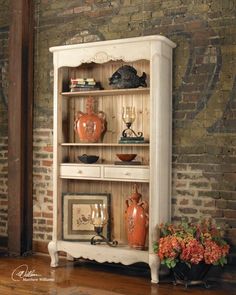 an old white china cabinet with orange vases on top