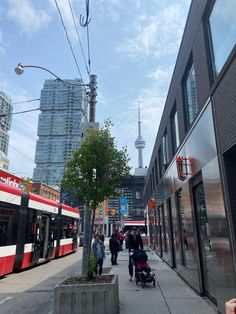 people are walking down the sidewalk in front of some buildings and a train on it