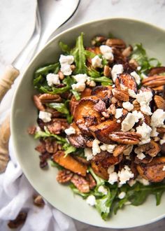 a salad with nuts and feta cheese in a white bowl next to a fork