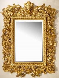 a gold framed mirror hanging on the wall next to a white wall with an ornate design