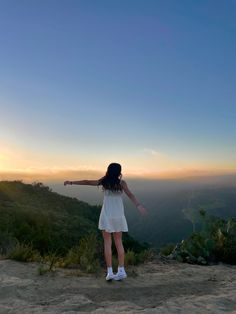 a woman standing on top of a hill with her arms outstretched