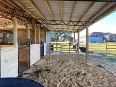 the inside of a horse barn with hay on the ground and horses in the background