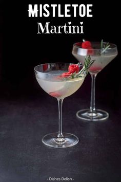 two martinis with garnishes sit side by side on a black surface