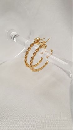 a pair of gold - plated hoop earrings on a clear glass stand with a white background