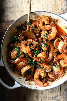 a pan filled with shrimp and spinach on top of a wooden table next to a spoon