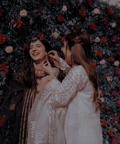 two women standing next to each other in front of a flower wall with roses on it