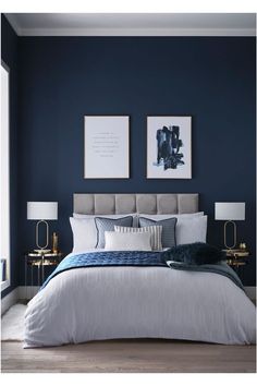 a bedroom with blue walls, white bedding and two framed pictures on the wall