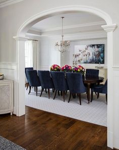 a dining room table with blue chairs and flowers on the top of it in front of an archway