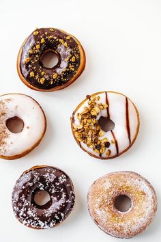 six donuts with different toppings are arranged on a white surface, top view