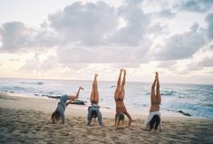 three women doing handstands on the beach in front of the ocean at sunset