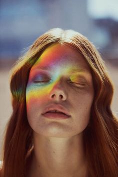 a woman with red hair and rainbow painted on her face is looking at the camera