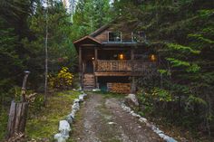 a cabin in the woods with trees and rocks on the path leading up to it