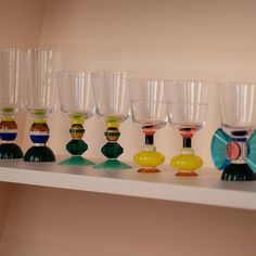 many different colored wine glasses lined up on a shelf in front of a white wall