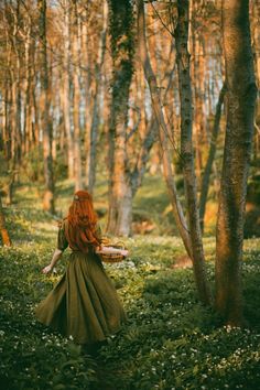 a woman with red hair is walking through the woods in a green dress and trees