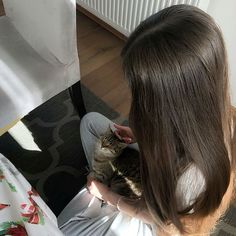 a woman sitting on the floor petting a cat with her hand in her lap