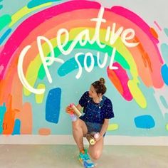 a woman sitting in front of a colorful wall with the words creative soul painted on it