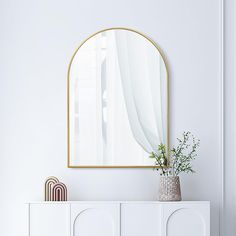 a white cabinet with a mirror on the wall above it and a plant in a vase next to it