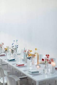 a long table is set with white chairs and flowers in vases on the tables