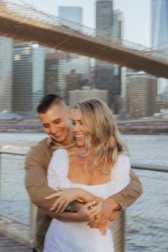 a man and woman walking across a bridge in front of a cityscape on the water