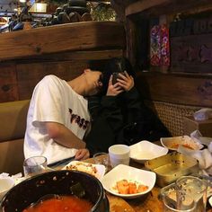 a man sitting at a table covered in food and drinking from a cup while covering his face