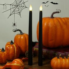 two candles are lit in front of some pumpkins and other halloween decorations on a table