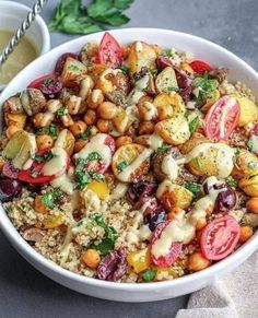 a white bowl filled with rice and vegetables next to a cup of sauce on the side