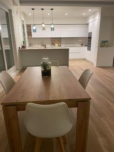 a wooden table sitting in the middle of a living room with white chairs and cabinets