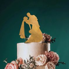 a wedding cake decorated with flowers and a gold silhouette topper on a green background