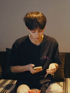 a boy sitting on a couch looking at his cell phone