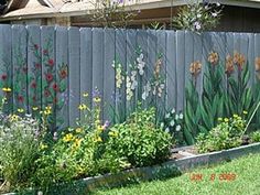 a fence with flowers painted on it and grass in the foreground, next to a flower garden