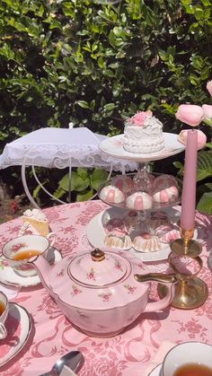 a table topped with plates and cups filled with cake next to a pink rose covered table cloth