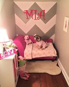 a small child's room with pink and gray walls, chevroned wallpaper and a dog on the bed