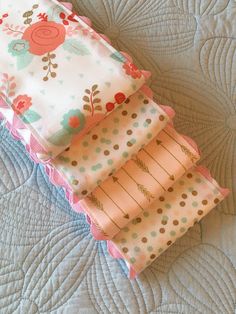 three pieces of fabric sitting on top of a quilted bed spread with pink and blue flowers