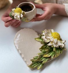 two flowers are placed on top of a heart shaped box and someone is holding it