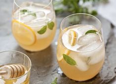 two glasses filled with lemonade and mint on top of a slate tray next to sliced lemons