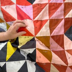 a person is cutting fabric with scissors and sewing needles on the quilts are colored red, orange, yellow, and black