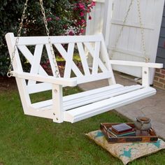 a white wooden swing sitting on top of a grass covered ground next to a potted plant