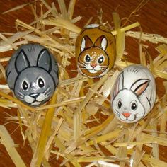 three painted easter eggs with faces of cats and rabbits on them sitting in some hay