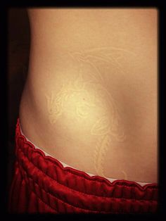 a woman's stomach with white tattoos on her body and red skirted pants