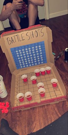 a man sitting on the floor next to a box with cups in front of it